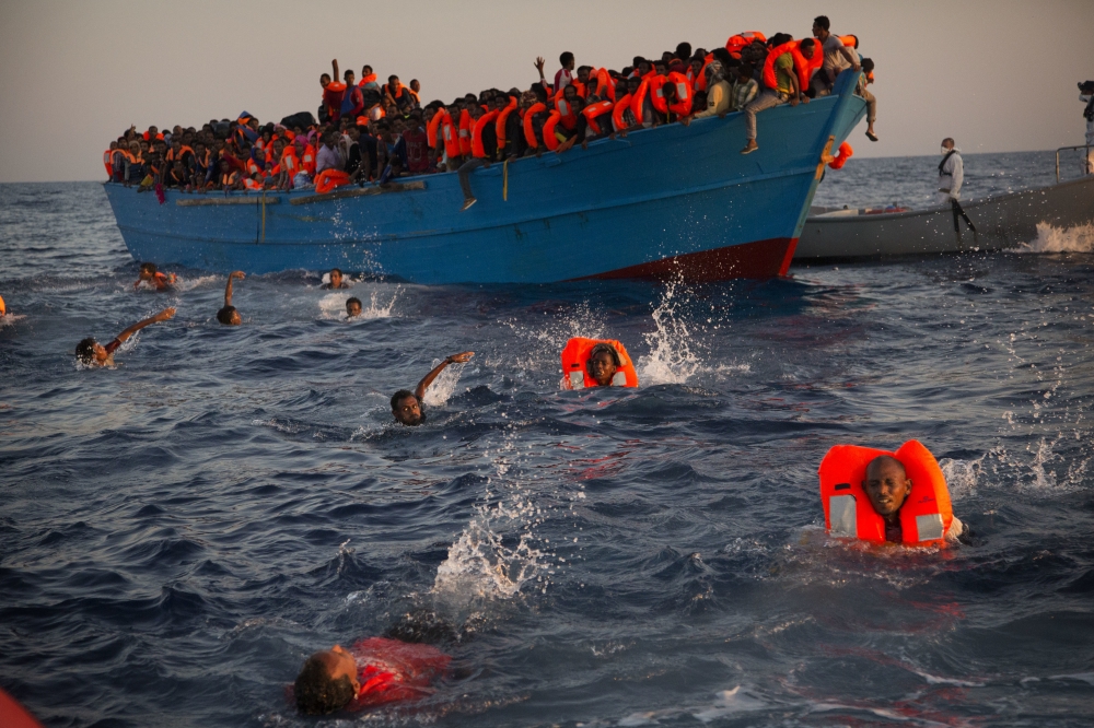 靠近利比亞海岸時，心急的難民見救援小組，逕自跳船游往救生艇。（美聯社）