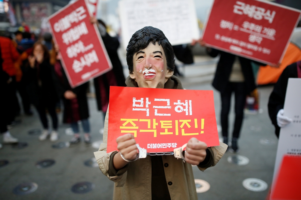 南韓民眾上街抗議，戴著諷刺朴槿惠的面具，手上的標語寫著：朴槿惠立刻下台。（湯森路透）
