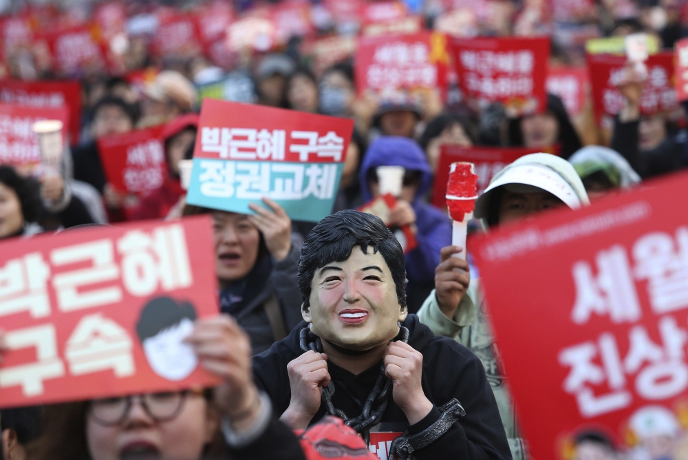 南韓一名民眾在抗議時戴著朴槿惠的面具。（美聯社）