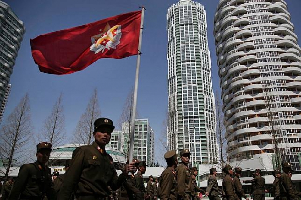 北韓士兵舉著國旗自平壤住宅大樓前經過。（美聯社）