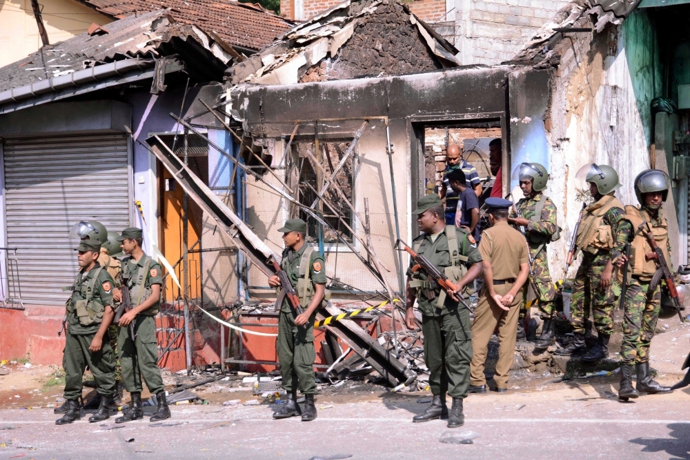 斯里蘭卡宗教衝突爆發後，數名軍警人員站在被燒毀的房子前。（湯森路透）