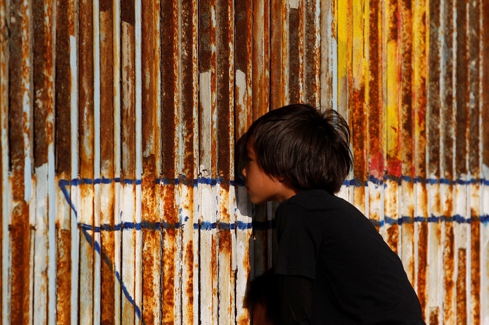 一名孩童隔著圍牆從墨西哥窺視美國。（湯森路透）