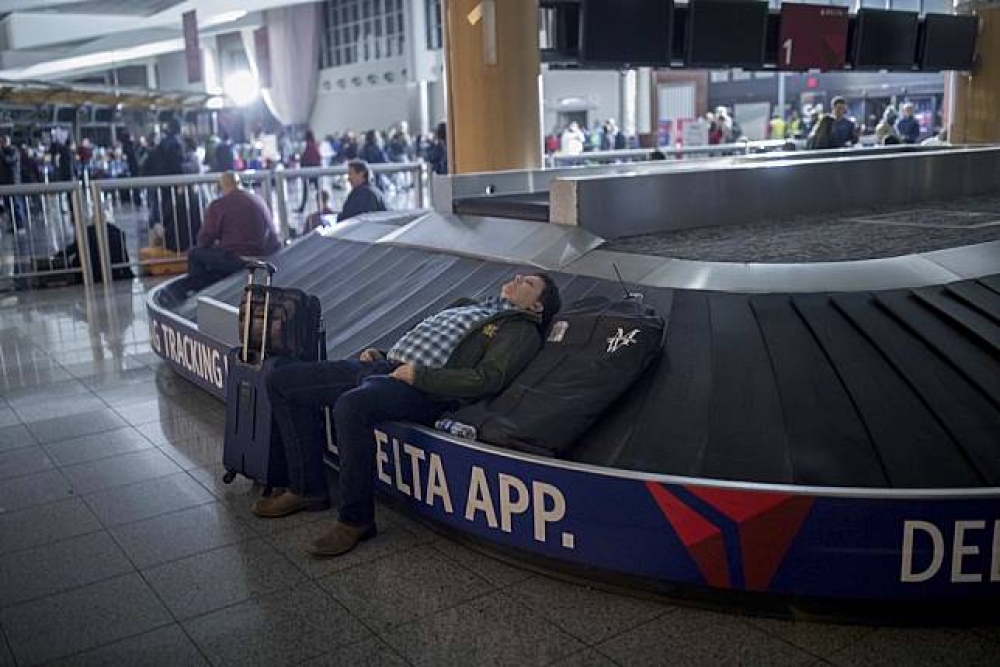 亞特蘭大機場停電後，一名旅客躺在行李輸送帶上睡覺。（美聯社）