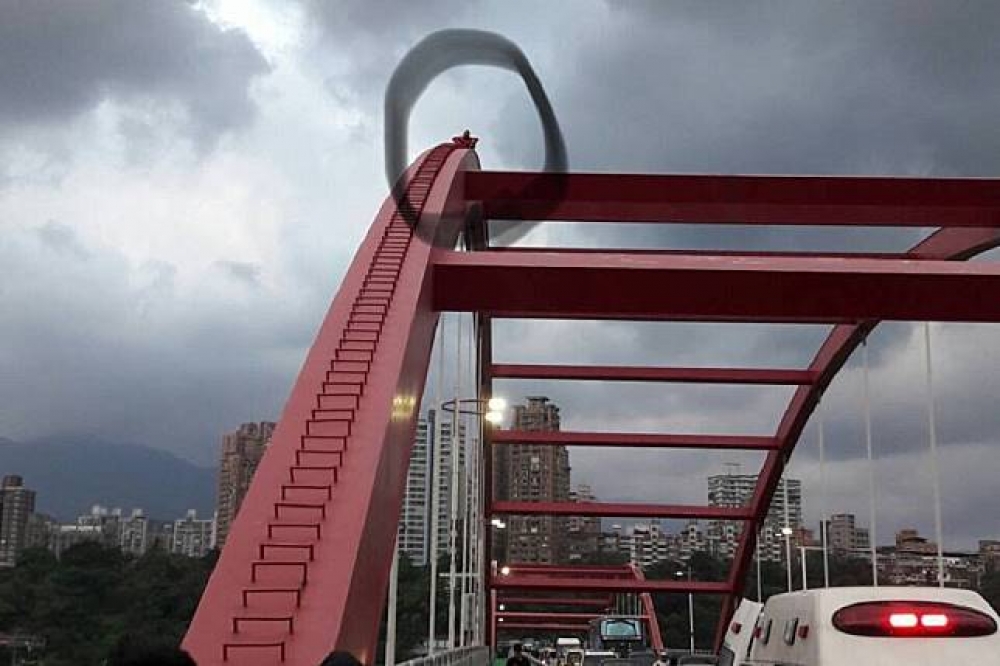 21日下午關渡橋上，1名紅衣男子爬上橋的頂端。圖中圈起處即是該名男子。（新北市消防局提供）