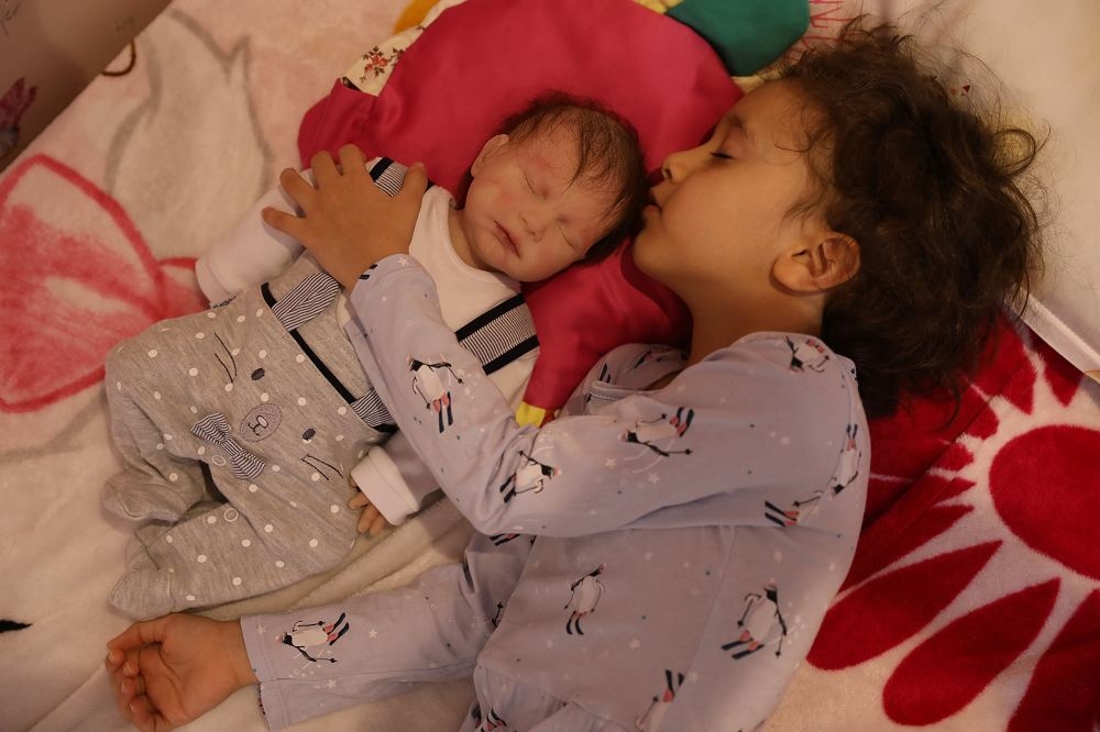 一名伊朗兒童巴蘭（圖右）陪著仿生的娃娃酣然入睡。（湯森路透）
