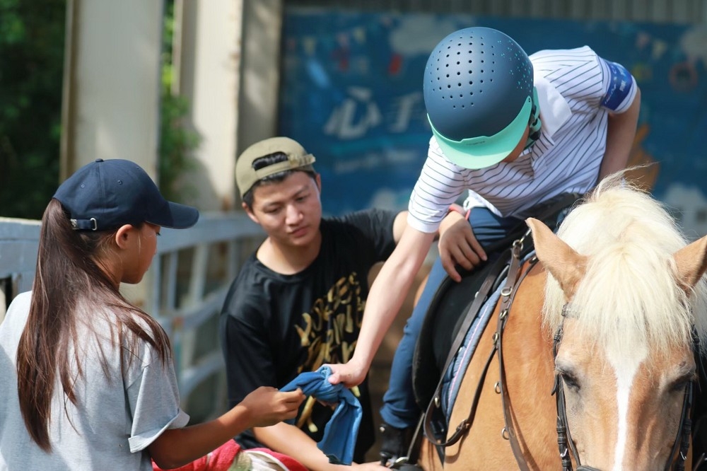 馬術志工服務隊協助腦麻兒童上馬。（桃園市青年局提供）
