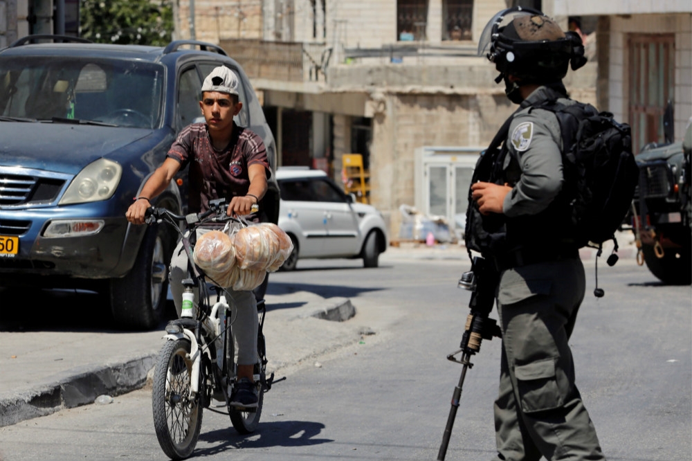駐守約旦河西岸屯墾區的以色列軍人與巴勒斯坦少年。（湯森路透）