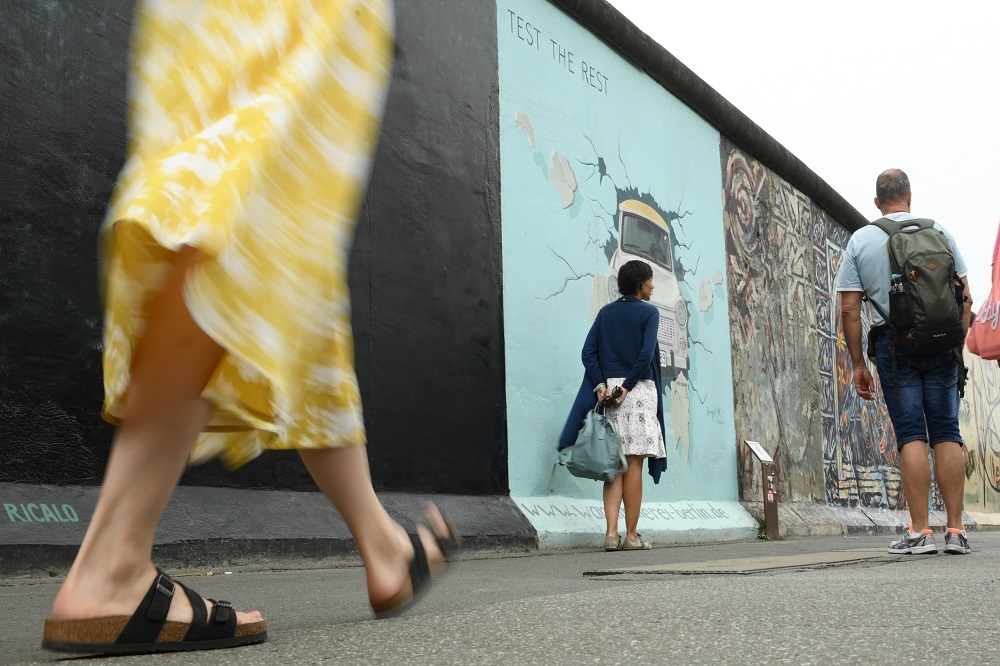 德國柏林圍牆舊址前走過的女性。（湯森路透）