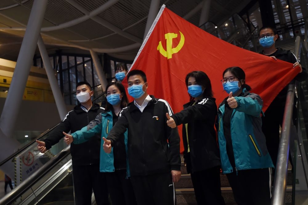 中國疫情趨緩，湖北省武漢市的支援醫護人員準備離去，18日於武漢車站內的中國國旗合影。（湯森路透）