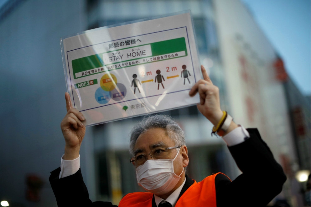 日本官員在東京鬧區舉牌提醒，民眾應保持社交距離。（湯森路透）