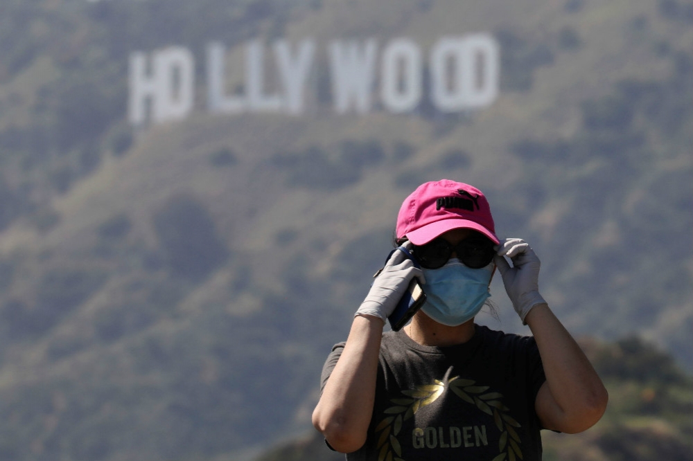 戴著口罩在加州地標「好萊塢」標誌前拍照的遊客。（湯森路透）