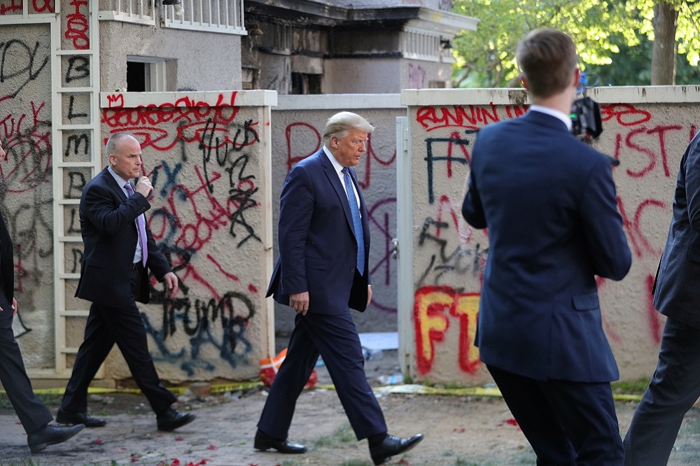 美國總統川普經過遭抗議民眾塗鴉的建築。（湯森路透）