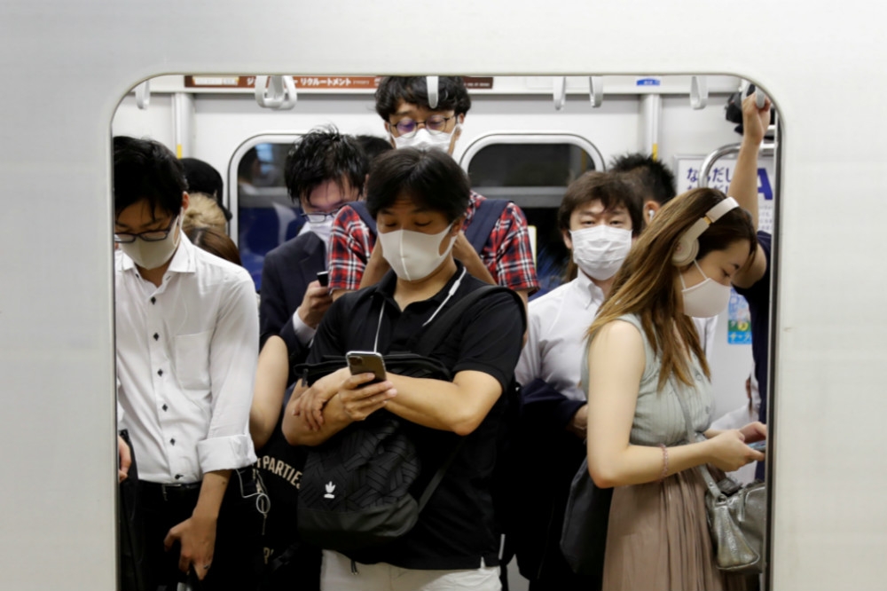 戴口罩擠上電車通勤的東京上班族。（湯森路透）