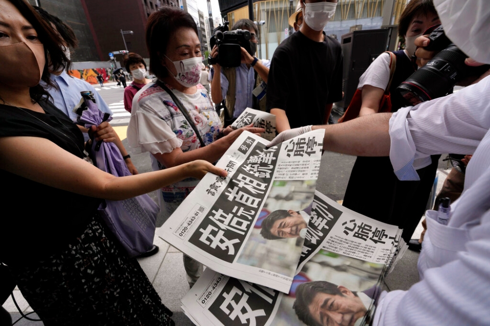 日本前首相安倍晉三8日上午中彈，當地媒體印製號外報紙，民眾立刻圍觀搶拿。（美聯社）