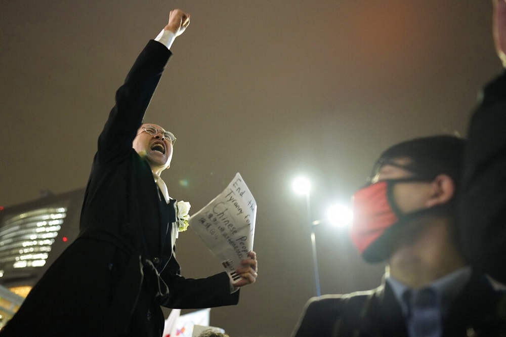 一名抗爭者在東京街頭，舉著標語聲援中國民主化。（美聯社）